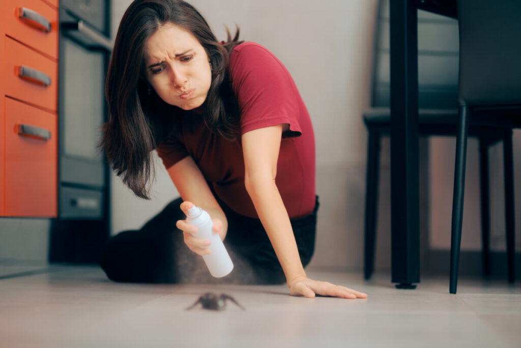 woman having a hard time spraying ant on the floor. whishes for pest control services